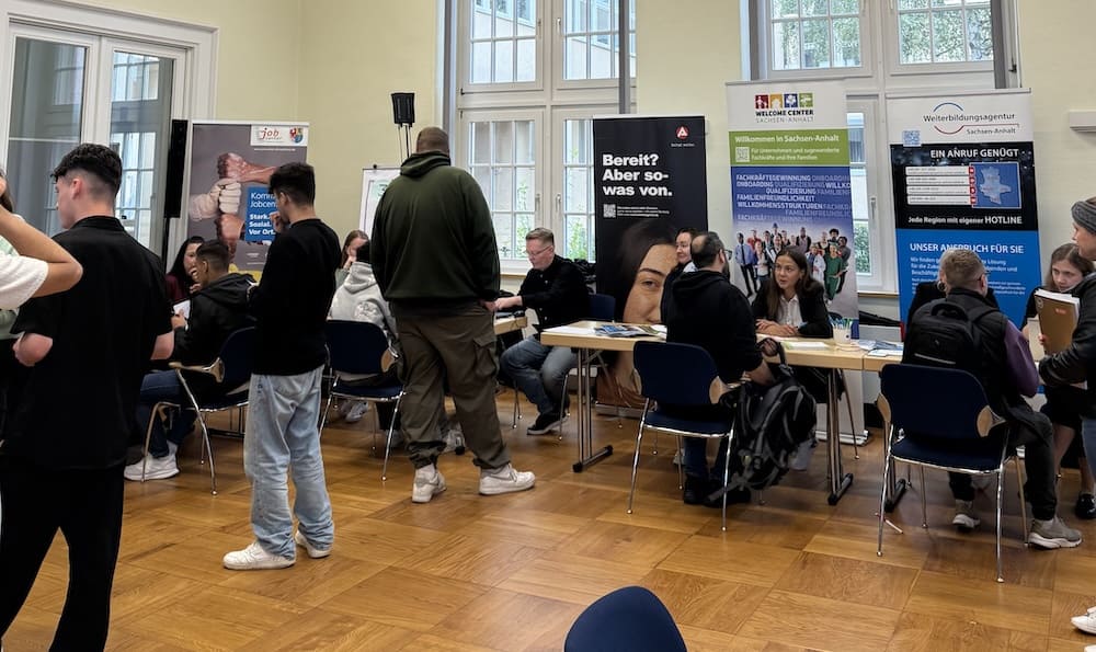 Besucher informieren sich an Ausstellungsständen bei einer Jobmesse in einem hellen Veranstaltungsraum.
